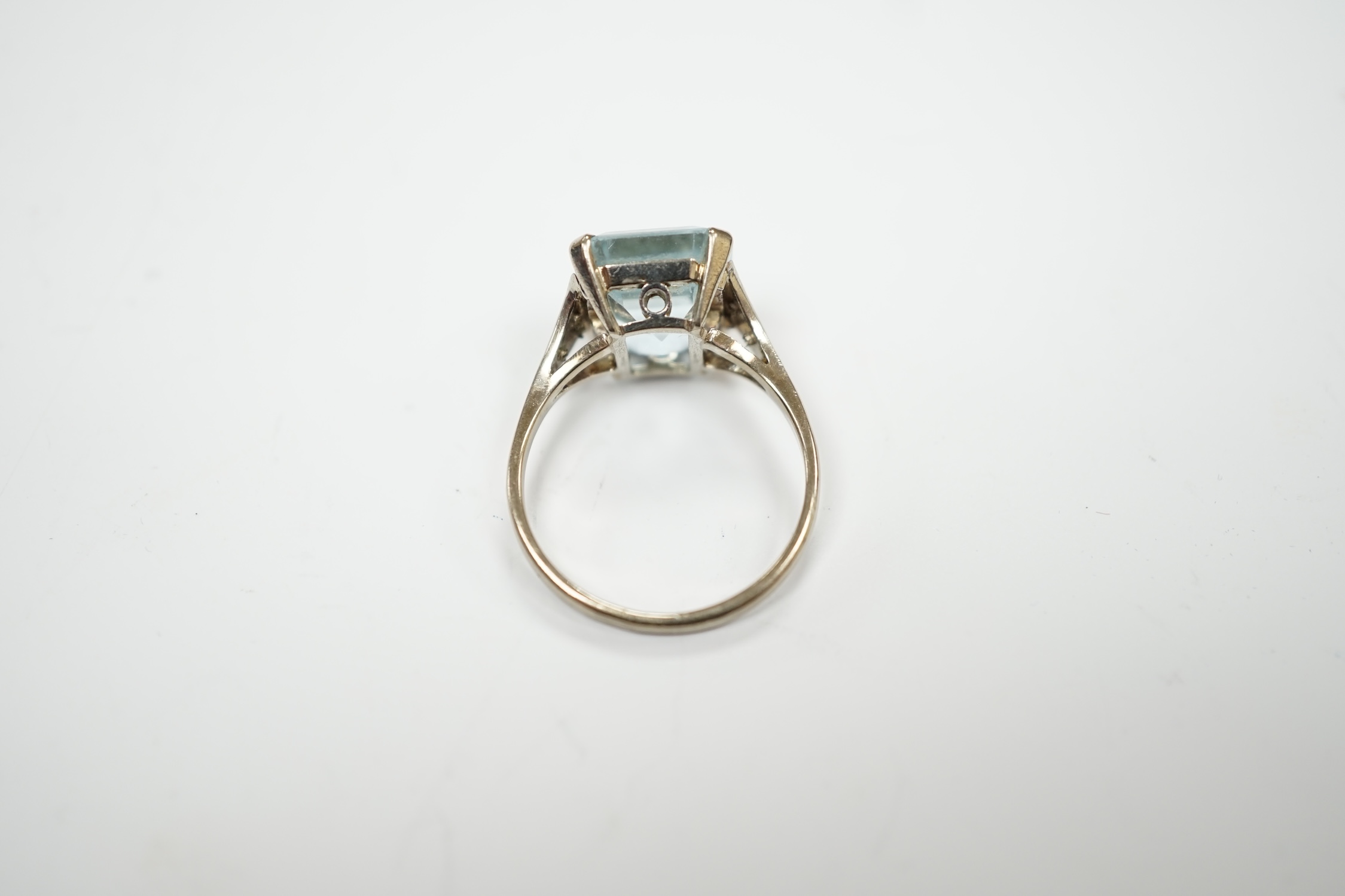 A white metal and single stone emerald cut aquamarine set ring, with rose cut diamond chip set shoulders (one stone missing), size M, gross weight 3.2 grams.